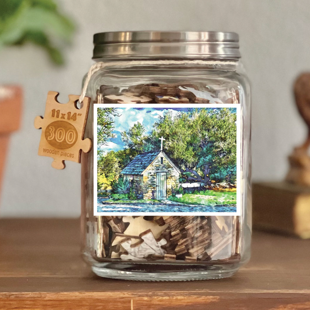 Image of puzzle shown on display clear glass Mason style jar with silver metal crew on lid. Exposes puzzle pieces inside the jar. Wooden tag hangs down the side of the jar with kite string from lid of jar with size and piece count engraved into it.