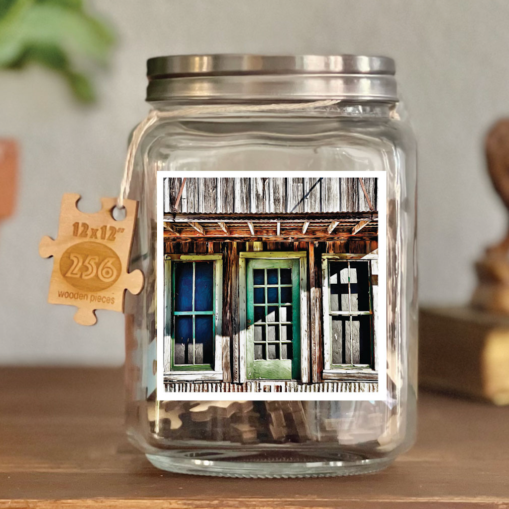 Image of puzzle shown on display clear glass Mason style jar with silver metal crew on lid. Exposes puzzle pieces inside the jar. Wooden tag hangs down the side of the jar with kite string from lid of jar with size and piece count engraved into it.