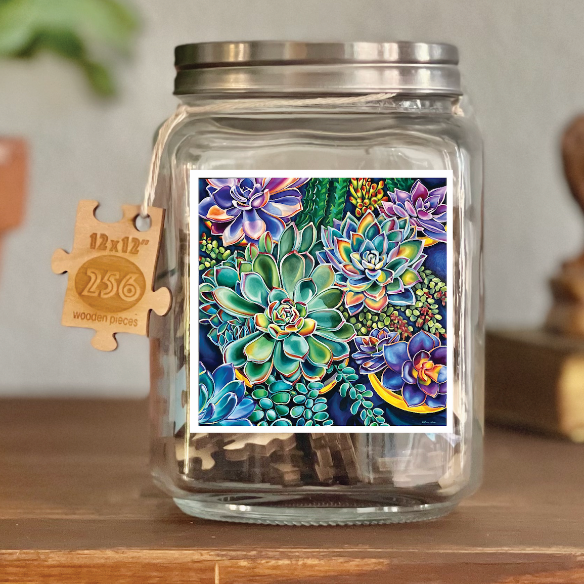 Image of puzzle shown on display clear glass Mason style jar with silver metal crew on lid. Exposes puzzle pieces inside the jar. Wooden tag hangs down the side of the jar with kite string from lid of jar with size and piece count engraved into it.